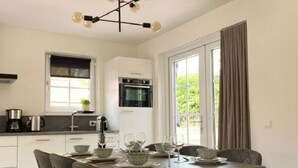 Une cuisine moderne avec des armoires blanches, un four encastré et un coin repas avec une table mise pour deux personnes.