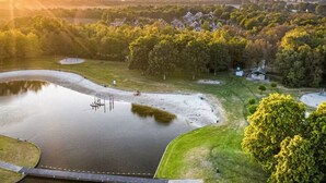 Une vue paisible sur un lac, avec un petit quai, entourée d’une végétation luxuriante et de bâtiments résidentiels en arrière-plan.