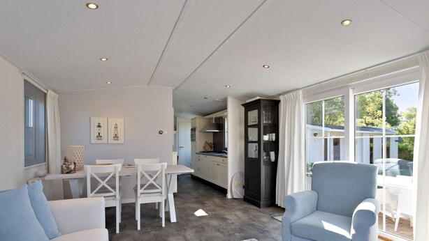 Sala de estar moderna com sofá, mesa de jantar com cadeiras, área de cozinha e uma grande janela com cortinas.