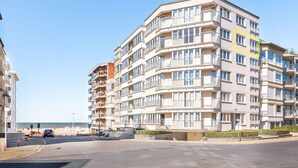 Un hotel de varios pisos con balcones, zona de estacionamiento y vista a la playa.