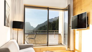 A modern living room with a sofa, a small coffee table, a TV, and a balcony with a mountain view. - Apartment in Schrocken Near Ski Arlberg (Schroecken)