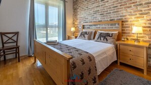 Une chambre à coucher avec un lit en bois, deux tables de chevet, une chaise et une grande fenêtre avec des rideaux.