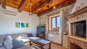 Un salon chaleureux avec une cheminée en pierre, un plafond en bois et un téléviseur posé sur un meuble en bois.