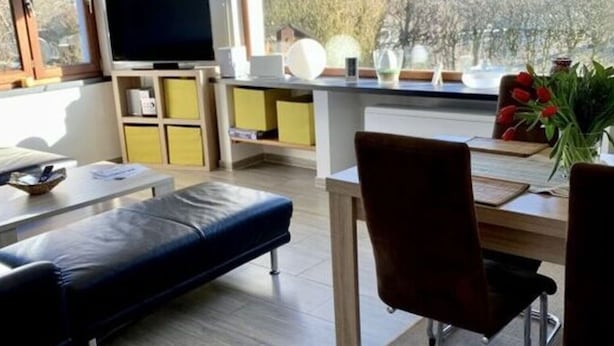 A modern living room with a sofa, dining table, and chairs. There is a TV and a window with a view of trees and mountains. - Deimann Modern Retreat (Schmallenberg)