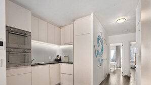 Une cuisine moderne avec des armoires blanches, un four encastré et un plan de travail agrémenté d’un bloc à couteaux et d’une bouteille.