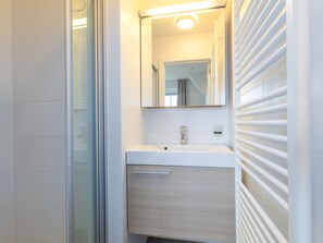 A modern bathroom with a glass shower enclosure, a white sink with a wooden cabinet, and a mirror above the sink. - Apartment With Cosy Sunny Terrace (Middelkerke)