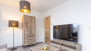 Ein modernes Wohnzimmer mit einem Holzkabinett, einem Fernseher auf einem Holztisch, einer Stehlampe und einem Couchtisch mit Dekorationselementen.