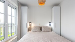 Ein Schlafzimmer mit einem großen Bett, zwei Nachttischen, einer Hängelampe und einem Fenster mit Vorhängen.