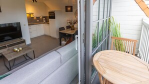 Eine moderne Küche mit weißen Schränken, ein Essbereich mit Tisch und Stühlen, ein Sofa und ein Fernseher.