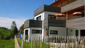 Uma casa moderna de dois andares com cerca de madeira, varanda com guarda-sóis e céu claro.