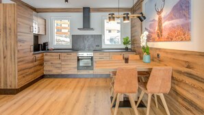 A modern kitchen with wooden cabinetry, a central island with seating, and a large window. - Golden Lodges Rauris Resort With Parking (Rauris)