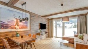 A modern living room with a wooden dining table, sofa, and a large TV mounted on the wall. - Golden Lodges Rauris Resort With Parking (Rauris)