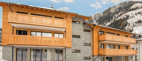 A modern multi-story building with wooden balconies, large windows, and a mountainous backdrop.