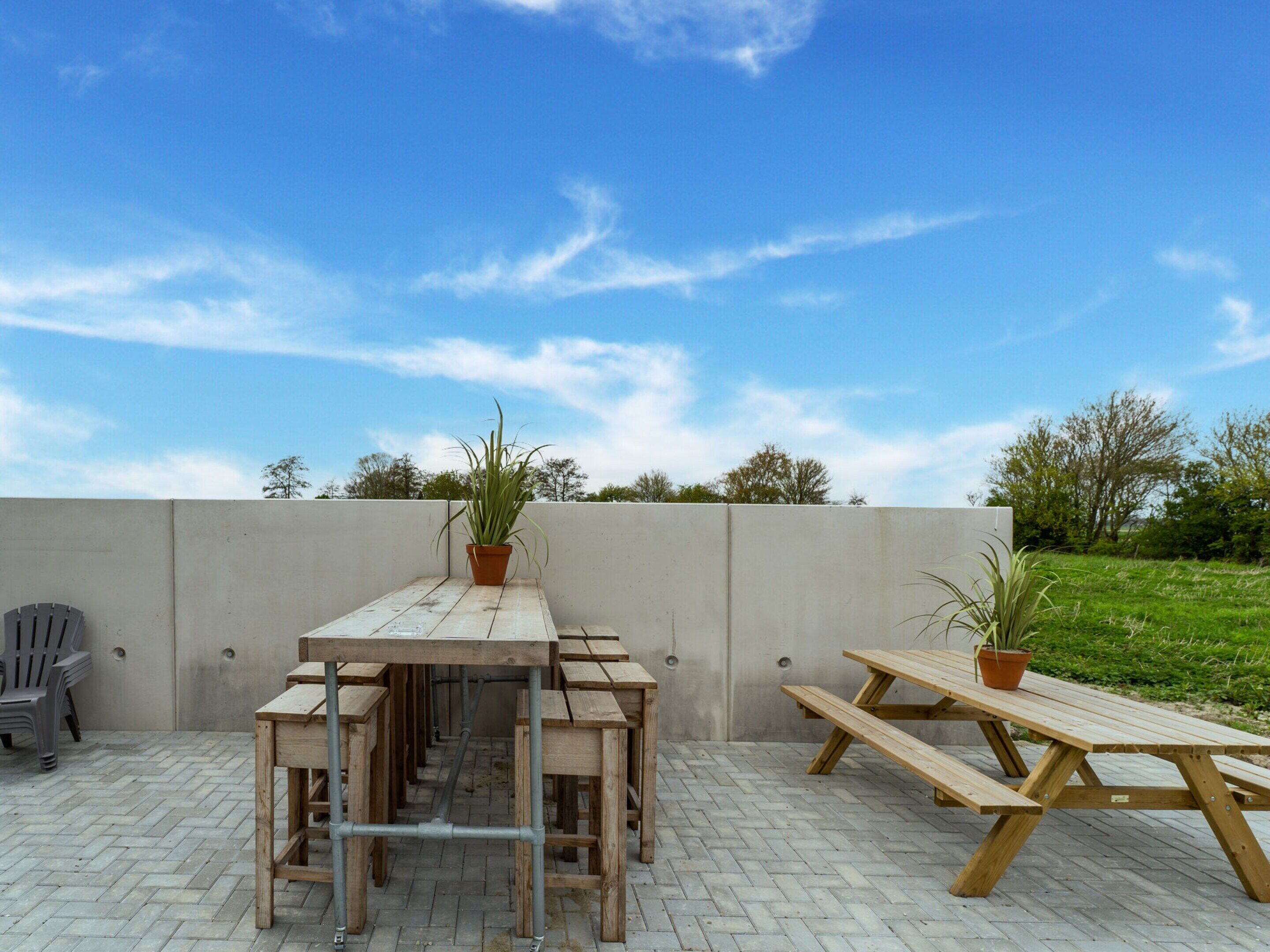 An outdoor patio with wooden tables and benches, potted plants, and a concrete wall.