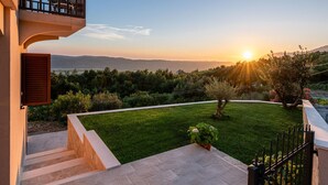 A residential property with a balcony overlooking a landscaped garden and a scenic view of the sunset over the hills. - Apartment in Konavle Region Gruda (Konavle)