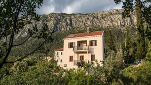 A two-story building with a balcony, surrounded by greenery and mountains in the background. - Apartment in Konavle Region Gruda (Konavle)