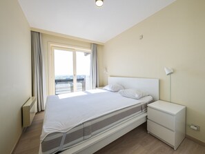 Een moderne slaapkamer met een enkel bed, een nachtkastje en een raam met gordijnen.