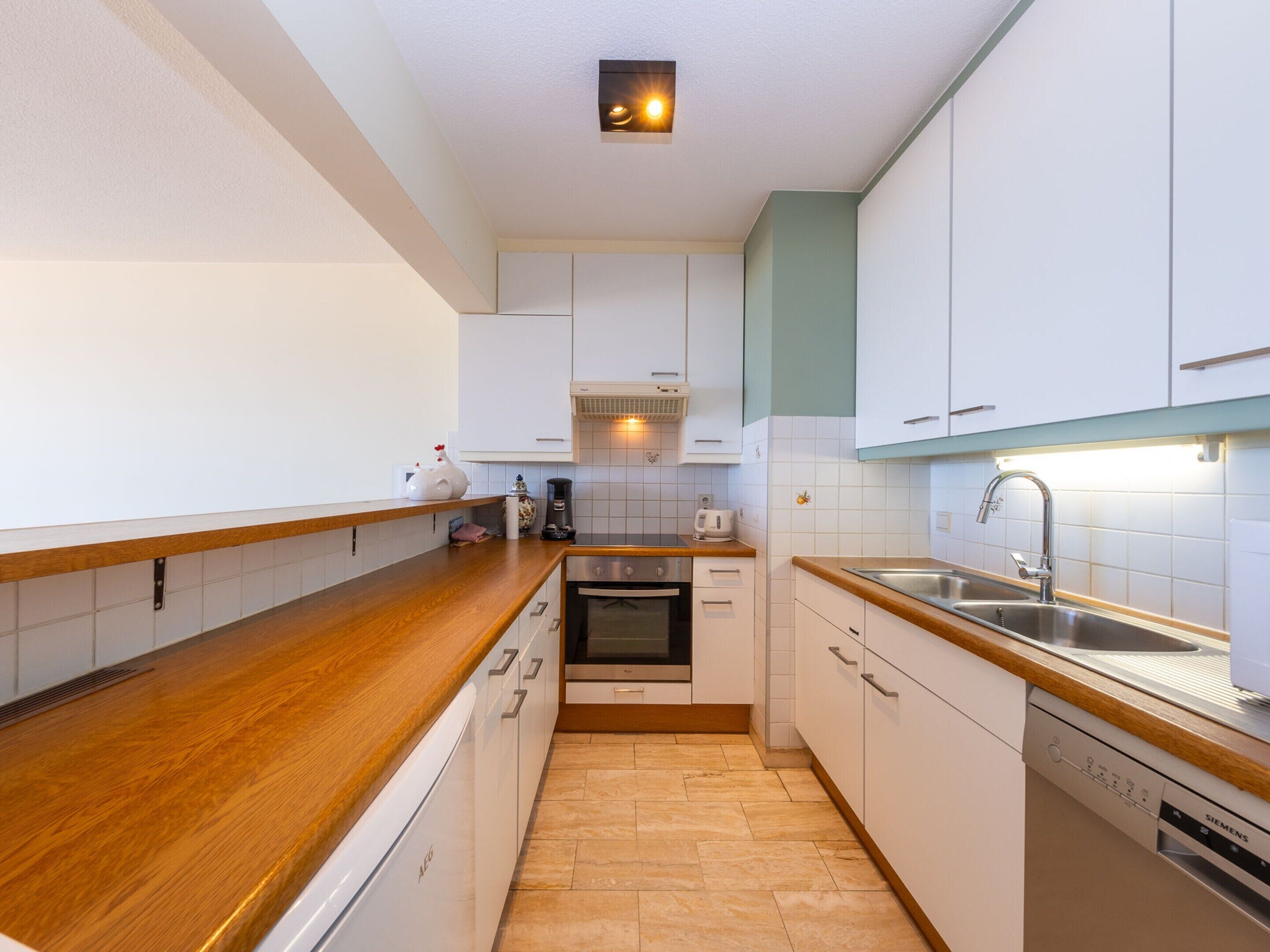A compact kitchen with white cabinets, a wooden countertop, a built-in oven, a dishwasher, and a sink.