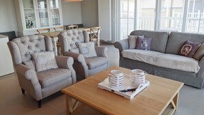 A living room with a grey sofa, two armchairs, a wooden coffee table, and a white cabinet with glass doors. - Apartment in Nieuwpoort Near the Beach (Nieuwpoort)