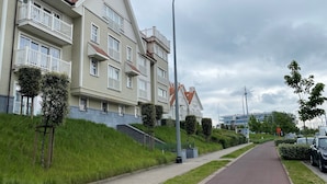 A residential building with multiple balconies, a paved pathway, and a street with parked cars. - Apartment in Nieuwpoort Near the Beach (Nieuwpoort)