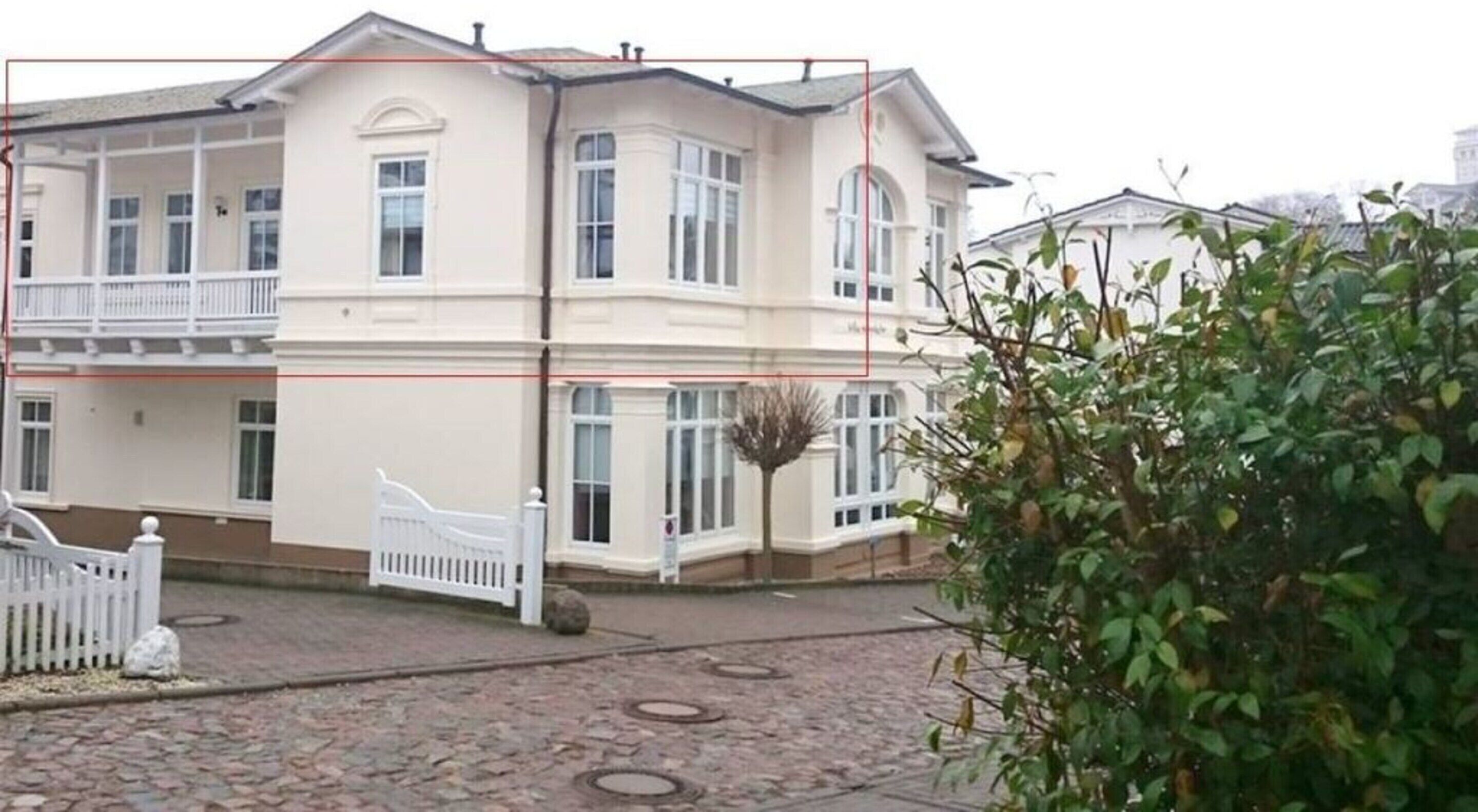 Ein zweistöckiges Gebäude mit weißer Fassade, zahlreichen Fenstern und einem verschlossenen Eingang.