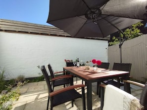 An outdoor patio with a wooden table and chairs, a large umbrella, and a white wall in the background. - Birklund Modern Retreat (Probsteierhagen)