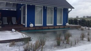 Ein blaues Haus mit einer überdachten Veranda, einem Swimmingpool und verschneiter Landschaft.