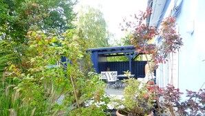 Eine Terrassenanlage mit Gartenmöbeln, umgeben von üppiger Bepflanzung und Topfpflanzen.
