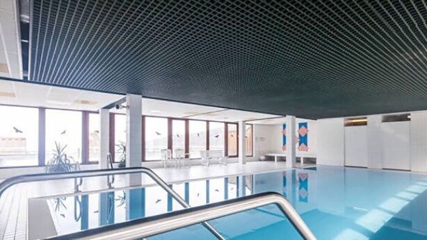 En inomhuspool med kristallklart blått vatten, omgiven av vita väggar och ett tak med ett rutmönster.