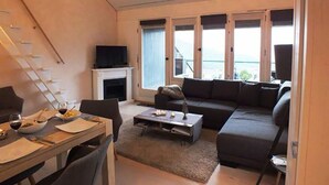 Ett modernt vardagsrum med en öppen spis, en soffa, ett soffbord och en matplats med ett bord och stolar.