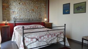 A bedroom with a stone wall, a metal bed frame, a red wall, and two framed pictures. - Apartment Milleluci 2 (Monforte d'Alba)