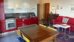 A compact kitchen with red cabinets, a dining table, and a red sofa in the living area. - Apartment Milleluci 2 (Monforte d'Alba)