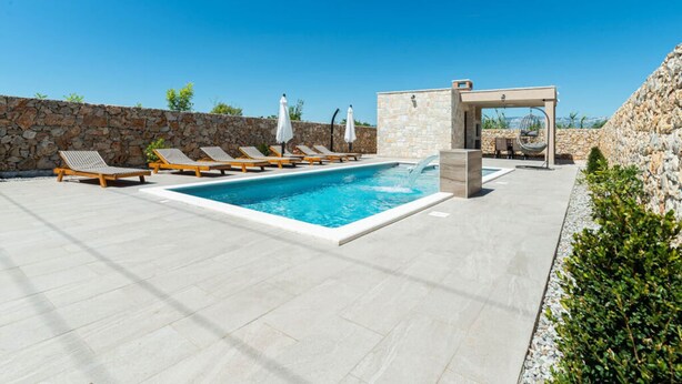 A pool area with lounge chairs, a stone wall, and a small seating area with a table and chairs. - With Pool, Jacuzzi and Sauna (Privlaka)