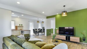 A modern living room with a green sofa, a TV, and a dining area in the background. - With Pool, Jacuzzi and Sauna (Privlaka)