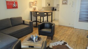 A modern living room with a grey sofa, black leather chairs, a coffee table with figurines, a wooden floor, a kitchen in the background, and a painting on the wall. - Apartment in Nieuwpoort Near the Beach (Nieuwpoort)