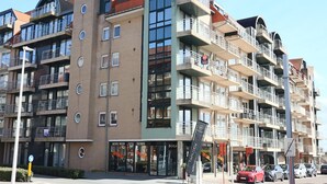 A multi-story building with balconies, a visible storefront, and a parking area. - Apartment in Nieuwpoort Near the Beach (Nieuwpoort)