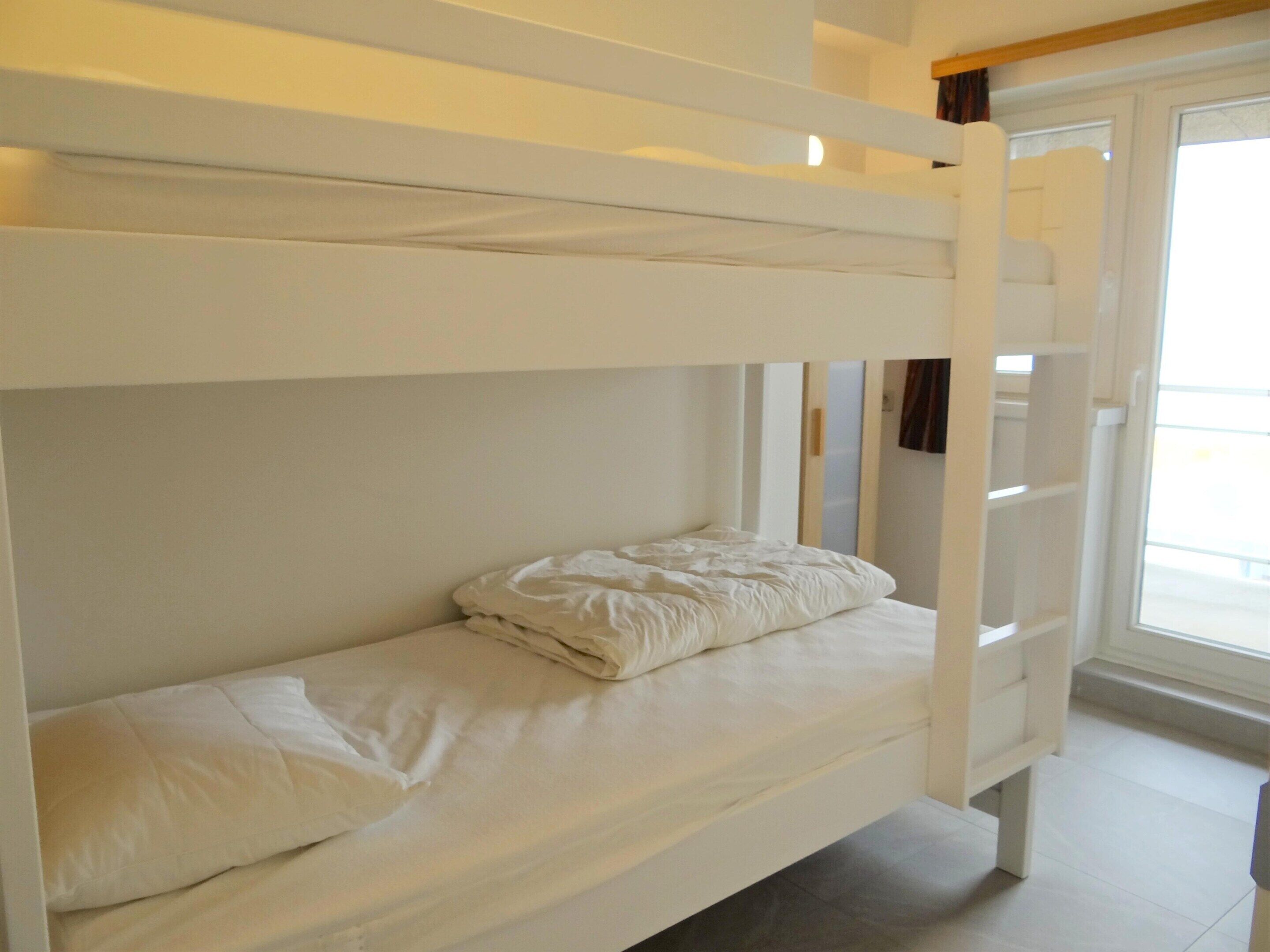 A bunk bed with white bedding in a room with a window and a door.