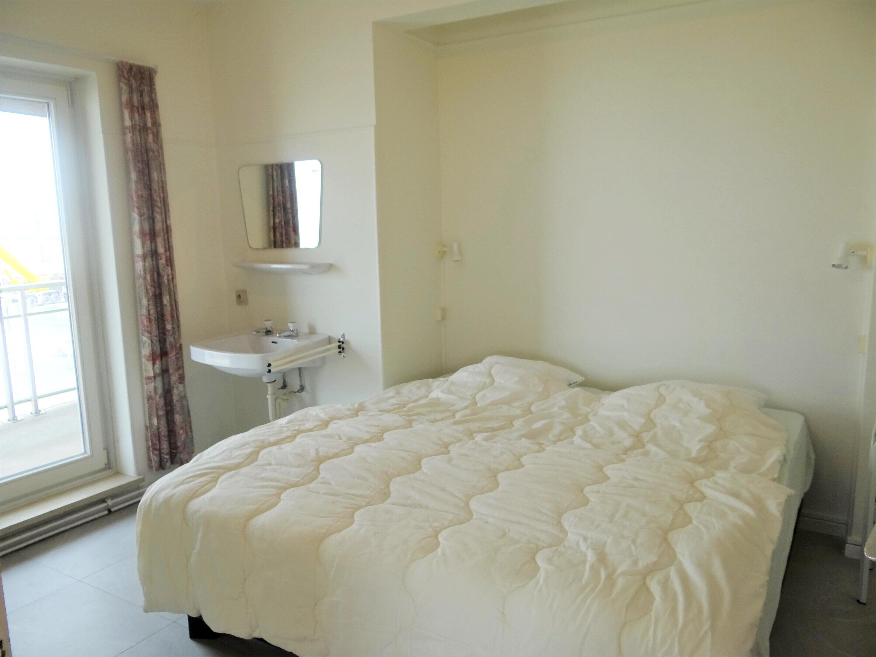 A bedroom with a bed, a window with curtains, a sink, and a mirror.