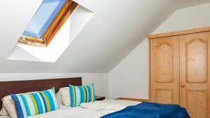 A bedroom with a sloped ceiling, a skylight, a bed with striped pillows, a blue blanket, and a wooden wardrobe. - Apartment in the ski and Hiking Area in Mallnitz (Mallnitz)