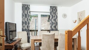 A room with a wooden table, four chairs, a television on a small table, patterned curtains, a clock on the wall, and a staircase. - Apartment in the ski and Hiking Area in Mallnitz (Mallnitz)