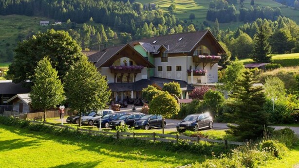 A traditional chalet-style hotel with a parking lot, surrounded by lush green hills and trees. - Apartment in the ski and Hiking Area in Mallnitz (Mallnitz)