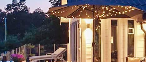 Une terrasse dotée de mobilier d’extérieur, d’un espace couvert agrémenté de guirlandes lumineuses et offrant une vue sur la maison.