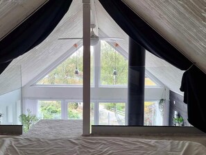 A high-ceilinged attic bedroom with a large window, a bed, and a ceiling fan. - 5 Star Holiday Home in Ronneby (Ronneby)