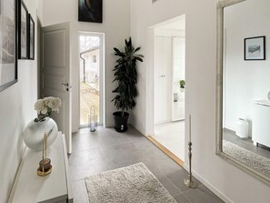 A hallway with a potted plant, a white vase with flowers, a rug, and a mirror reflecting a bathroom. - 5 Star Holiday Home in Ronneby (Ronneby)