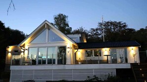 Een modern huis met een grote glazen gevel, een schuin dak en een overdekte veranda.