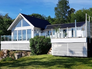 Una casa moderna con un amplio ventanal, un balcón y un panel solar.