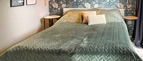 A bed with a green textured bedspread, a floral wallpaper, and two bedside tables with lamps.