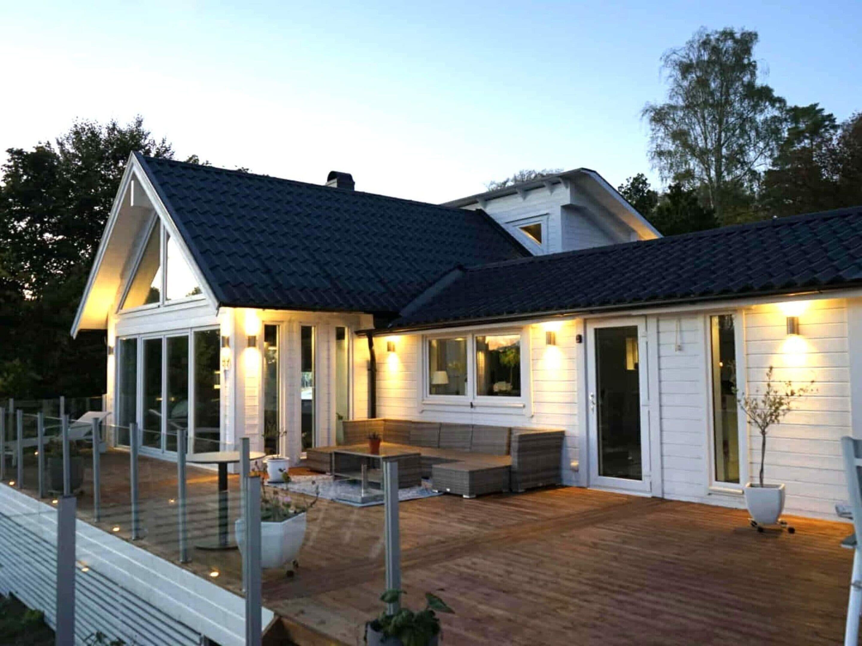 A modern house with a covered patio, large windows, and a well-lit exterior.