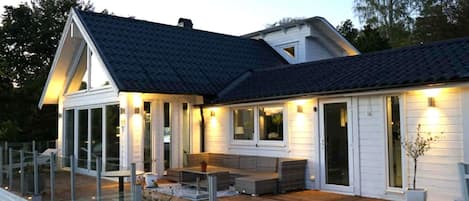 A modern house with a covered patio, large windows, and a well-lit exterior.