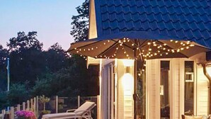 Une terrasse dotée d’une chaise longue, de mobilier d’extérieur et de guirlandes lumineuses.